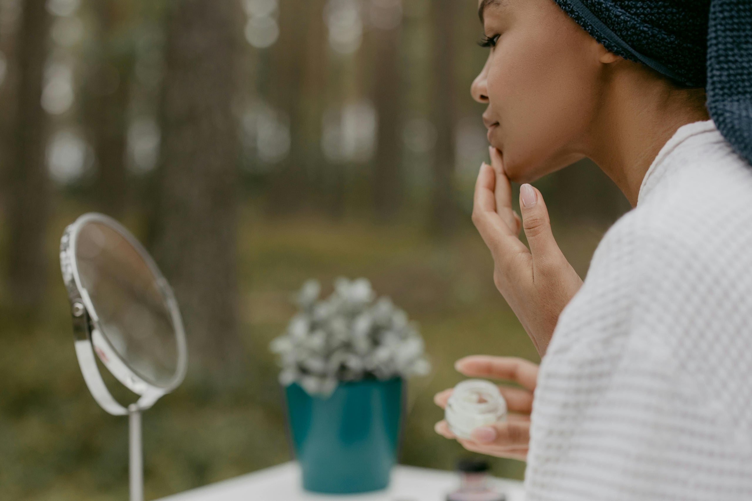 Woman applying makeup outdoors with a mirror and plant in the backgroundslider_item_qf8hyd